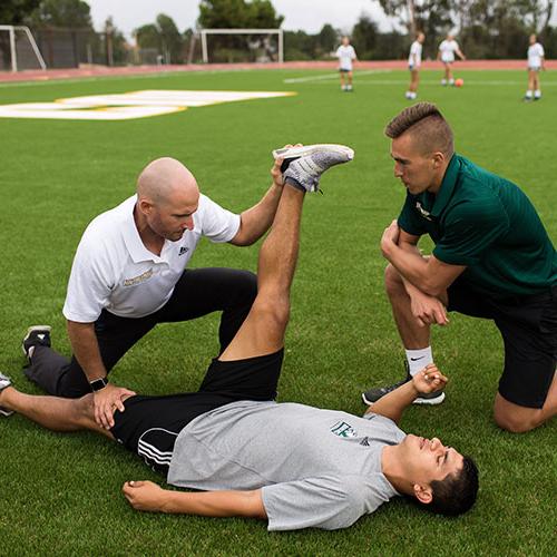 运动教练帮助足球运动员伸展